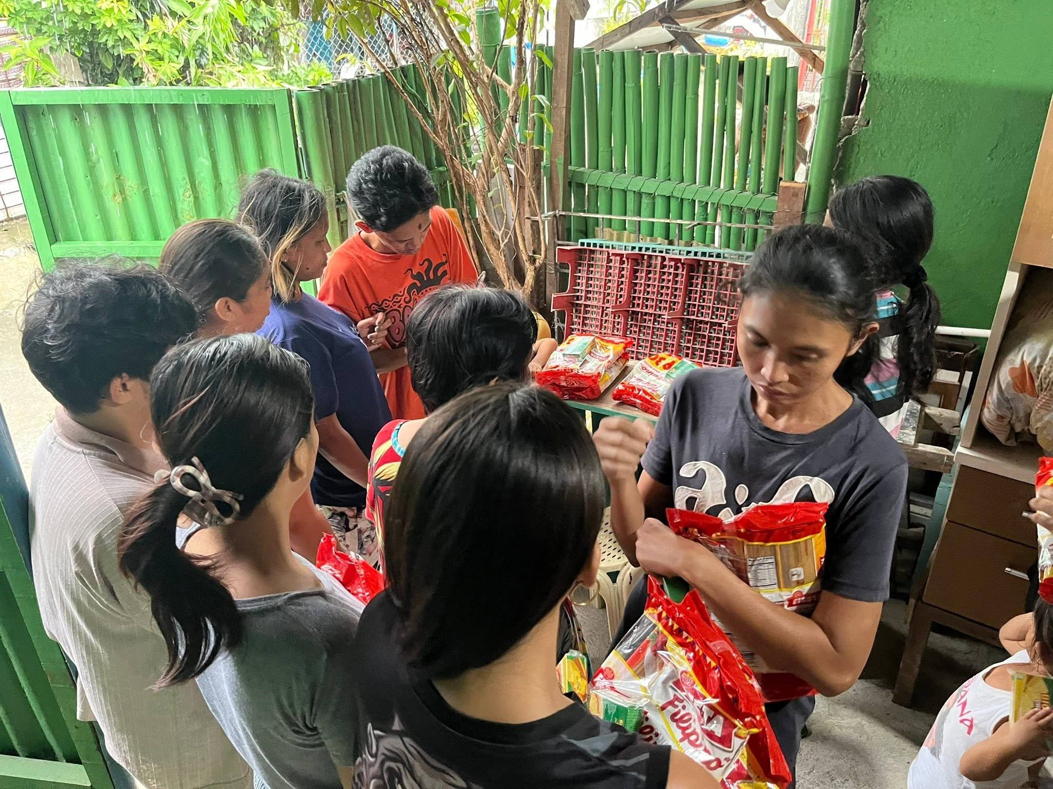 Neighbours, many of them young, crowd around the red spaghetti packs at the distribution point.