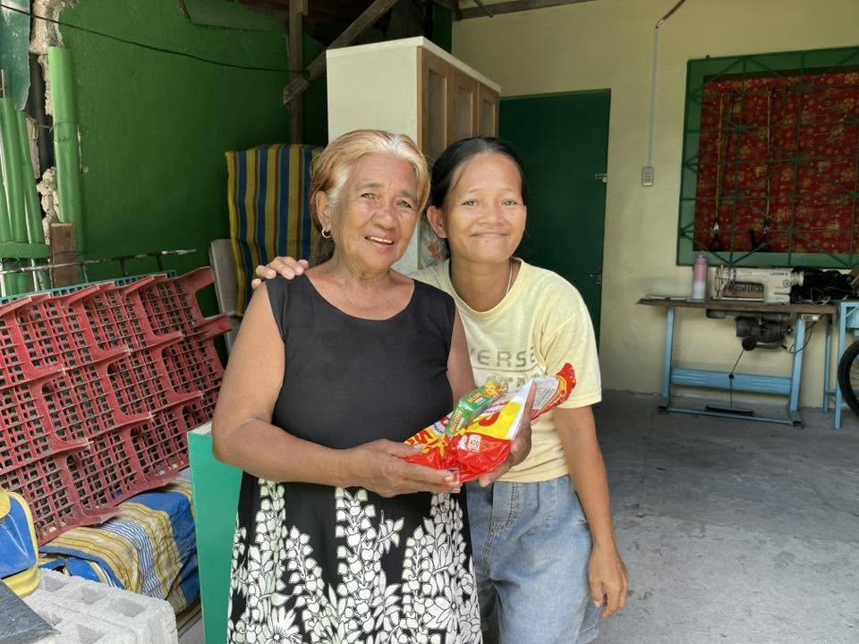 An older woman and a younger woman lean in close, smiling, holding one spaghetti pack between them.